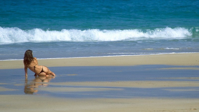 žena na pláži v bikinách, more za ňou